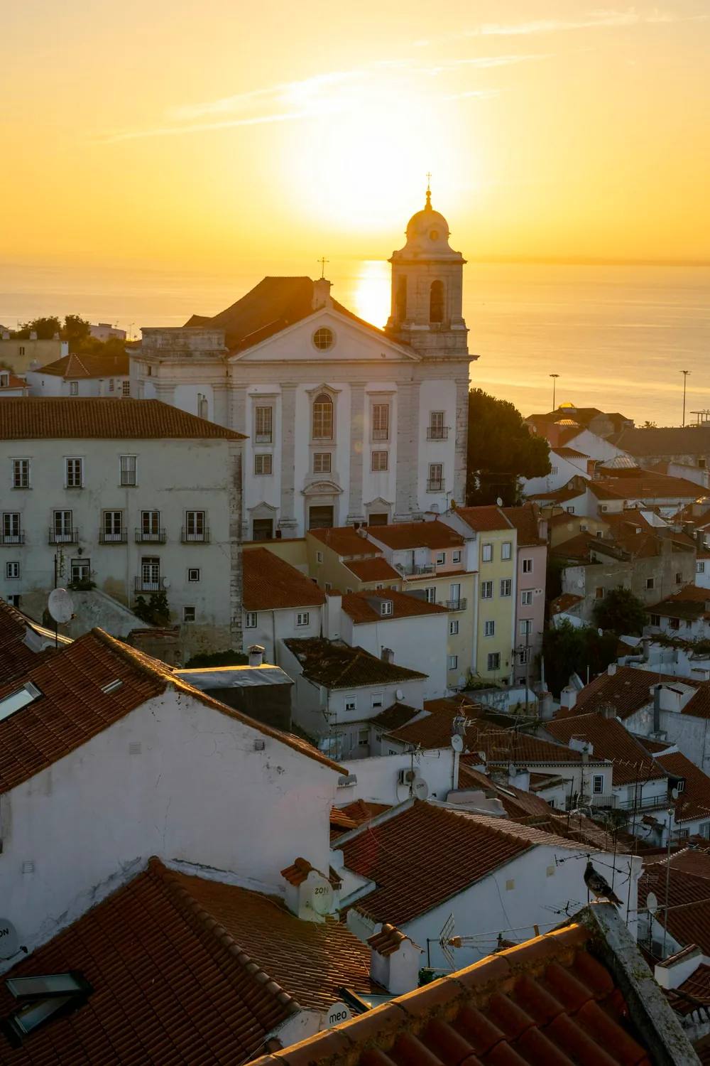 Pôr do sol sobre os telhados e a torre de uma igreja em Alfama, Lisboa